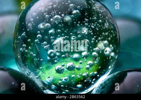 Close up macro shot of marbles. Glass sphere with air bubbles reflecting in the transparent teal blue coloured smooth surfaced stone. Stock Photo