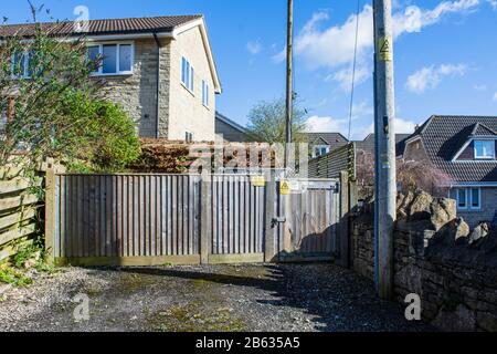 A wooden fence with padlocked gate and warning signs around an electricty substation in the middle of a housing estate Stock Photo