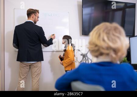 Male teacher writing on whiteboard, explaining programming Stock Photo