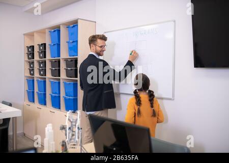 Male teacher writing on whiteboard, explaining, smiling Stock Photo