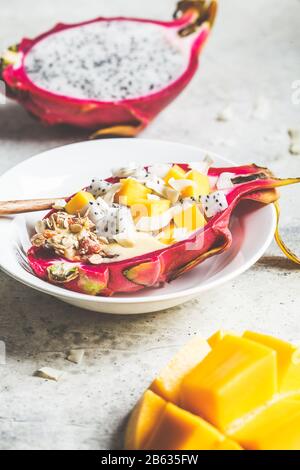 Mango smoothie with granola and coconut chips in dragon fruit. Healthy breakfast concept. Stock Photo