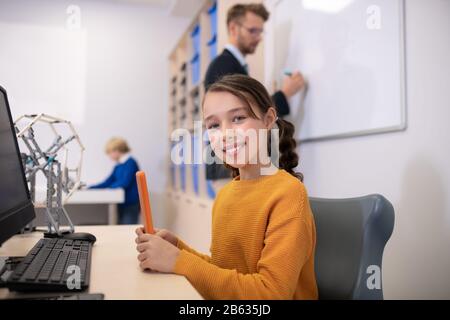 Male teacher writing on whiteboard, girl sitting at the desk, boy standing in background Stock Photo
