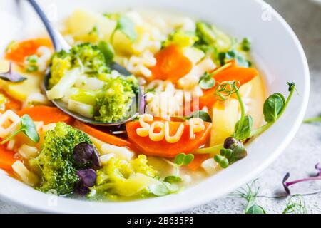 Healthy kids alphabet soup with vegetables and noodle letters in white plates. Baby food concept.