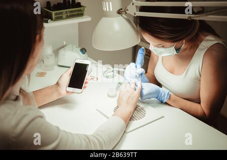 Manicure procedure. Smartphone in hands of client. Beauty salon Stock Photo