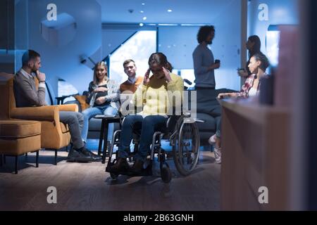 Handicapped young woman with colleagues working in office. Performing in co-working space. Office people working together. Stock Photo