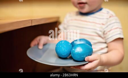 hands of small child hold plate with blue eggs. colouring eggs for eastertime at home for spring religious holiday. Copy space Stock Photo