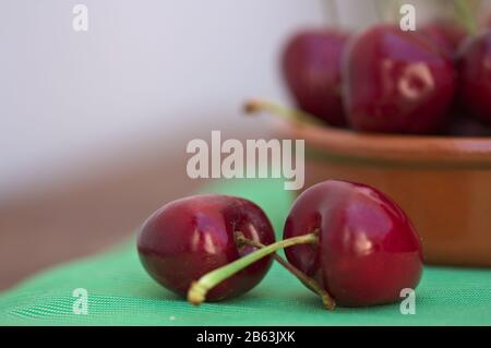 Cherries with their stems crossed on a green table and a blurred bowl in the background and space for texts Stock Photo