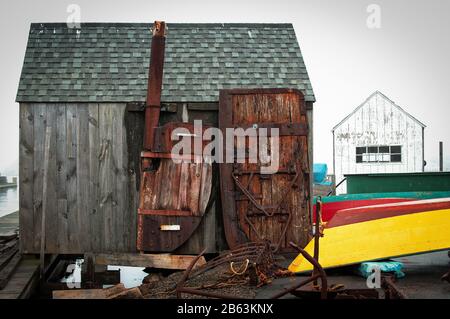 The focal point of the image is a weather-worn gray wood shack perched on the dock. Two brightly colored wooded skiff boats are dry-docked Stock Photo
