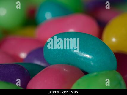 A large teal jelly bean stands out in a colourful pile Stock Photo