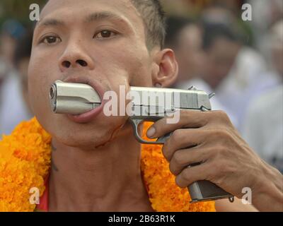 Thai Chinese Taoist devotee (mah song) pierces his left cheek with the barrel of an automatic pistol during the Phuket Vegetarian Festival. Stock Photo