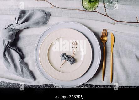 Eco-friendly natural table setting. Two white vintage plates with a gold fork and a gold knife and a cotton blue-gray napkin on a white vintage tablec Stock Photo