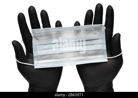 Doctor holds surgical face mask in hands in black medical gloves. Isolated on white background. Pandemic insurance, airborne diseases, SARS, influenza Stock Photo