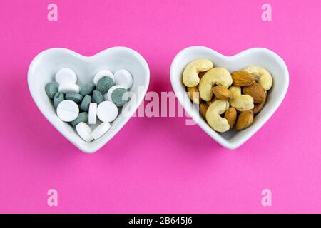Health concept, nuts against pills stand in salad bowls on a pink background. Top views Stock Photo