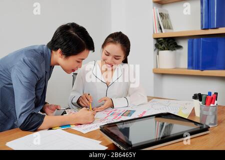 Smiling team of UX and UI designers discussing project details at meeting and choosing color palette Stock Photo