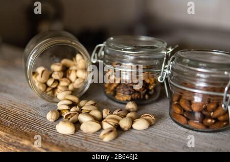 Pistachios scattered on the white vintage table from a jar and with other nuts on background. Pistachio is a healthy vegetarian protein nutritious Stock Photo