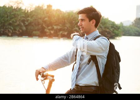 Young entrepreneur using virtual assistant in his smart watch when riding electric kick scooter Stock Photo