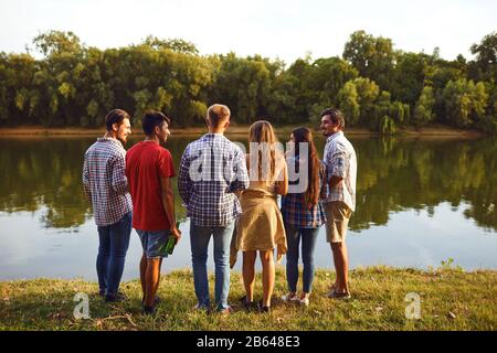 Back view a group of young people resting, communicates on the lake Stock Photo