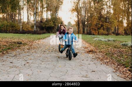 Charming caucasian siblings are having fun during an autumn walk in the park while riding their bikes