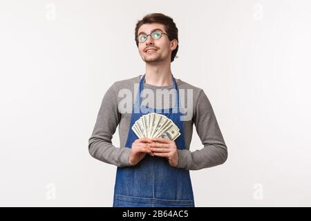 Small business, finance and career concept. Portrait of dreamy and pleased, handsome young man in apron, working at coffee shop or restaurant in apron Stock Photo