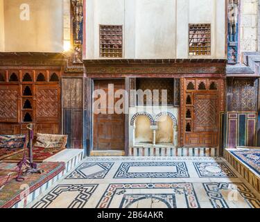 Wooden painted floral patterns, embedded arched niche, wooden door, wooden engraved cupboard, calligraphy decoration, and marble floor with geometric pattern at El Sehemy ottoman era historic house  Stock Photo