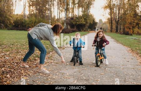 Caucasian mother having fun with kids during a walk with bikes in the park Stock Photo