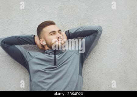 Bearded man holding hands behind head dreaming on a gray background. Stock Photo