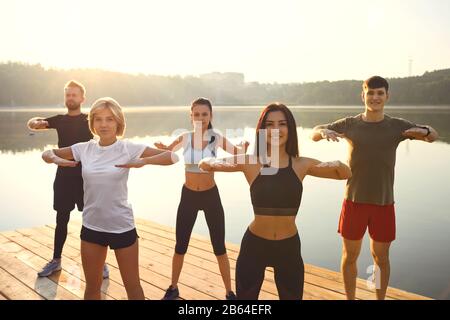 A group of active people do exercises in the park near the lake. Stock Photo
