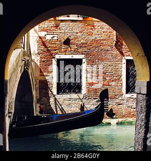The ferro on the bow of a Gondola passing under canal bridge on canal street Venice Italy Stock Photo