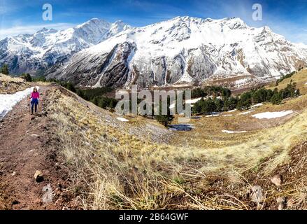 Hiker woman walking on mountain trail with hiking sticks, looking at view in Elbrus region, Caucasus mountains Stock Photo