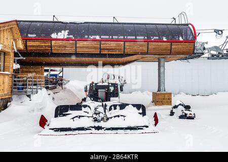 Snowcat after snowfall on slope in the mountains at skiing resort Elbrus, standing near cable way and snowmobile Stock Photo