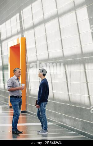 Businessmen meeting in office corridor during coffee break and discussing news and fresh ideas Stock Photo