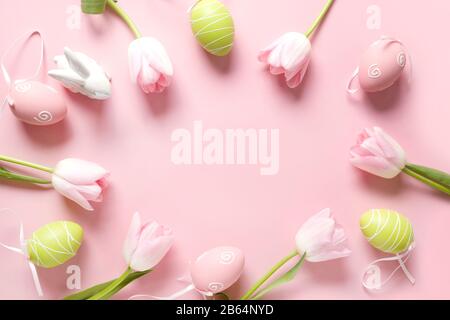 Easter frame of fresh pink flowers, bunny, colorful eggs and bunny on pink. Top view with copy space. Happy Easter holiday. Greeting card. Stock Photo