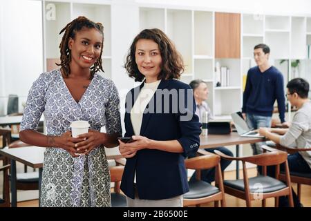 Portrait of smiling pretty successful businesswomen with coffee and smartphone looking at camera Stock Photo
