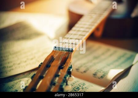 An old acoustic guitar, illuminated by bright sunlight, is lying on the table near the sheets of notes from the melodies. Stock Photo