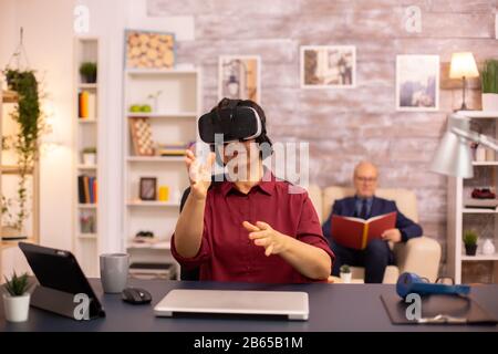 Old elderly woman using a VR virtual reality headset for the first time in her house. Concept of active elderly people using modern technology Stock Photo