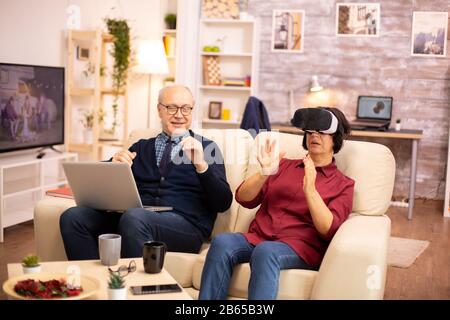 Old elderly retired woman in her 60s experiencing virtual reality for the first time in their cozy apartment Stock Photo