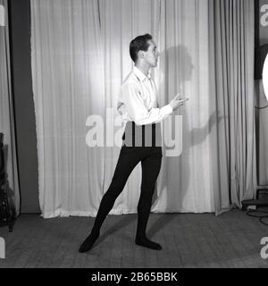 1950s, historical, picture of a slim build male ballet dancer in shirt and tights, practising his moves on a wooden stage in front of a curtain, England, UK. Stock Photo
