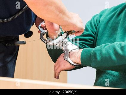 10 March 2020, Schleswig-Holstein, Lübeck: An accused prisoner sits in the regional court in the hall and has his handcuffs removed. The man is said to have taken a psychologist hostage and threatened her with a knife in June 2019 in the Lübeck prison in order to force his deportation to Romania. (to dpa 'Trial against suspected hostage-takers from Lübeck prison begins') Photo: Daniel Bockwoldt/dpa Stock Photo