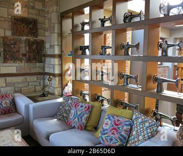 Partial view of living room decorated with collection of vintage sewing machines on a bookshelf and colourful sofas with cushions. Stock Photo