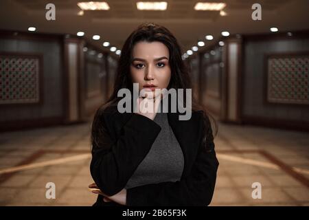 dramatic portrait of a beautiful young woman in a black coat in an underground passage.mosaics on the walls are not someone's works of art.these are w Stock Photo