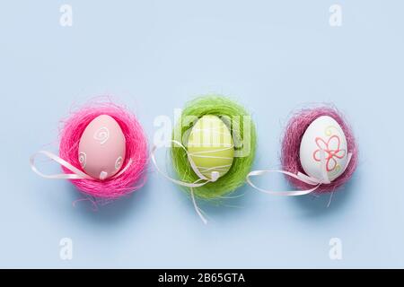 Colorful pastel eggs in three nests. Easter minimal creative composition on blue. Happy holiday. Greeting card. Stock Photo