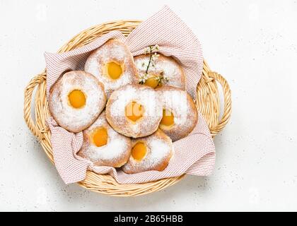 Top view of homemade easter dough bread rolls apricot and powdered sugar in a basket on a white table. Copy space. Stock Photo