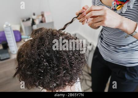 Close up of a hairdresser curling short black hair with hair irons. Stock Photo