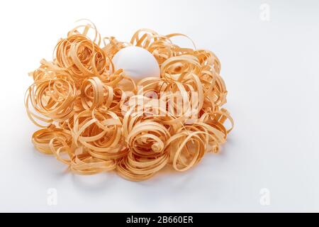 A patten of a white egg decorated with wood sawdust like a nest for Easter on a white background Stock Photo