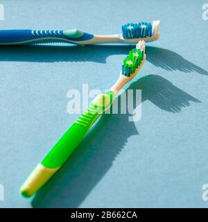 New multicolored toothbrushes with sharp shadows lie on a blue background. Close-up Stock Photo
