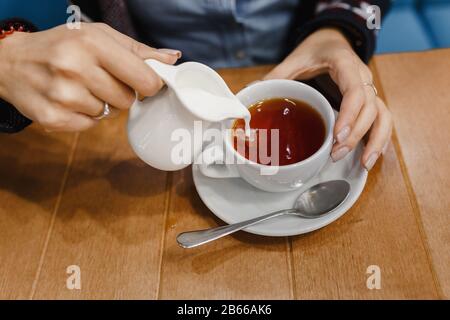 Woman pouring milk in mug of tea from kettle Stock Photo