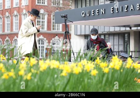 A journalist wearing a face mask, possibly in light of the Coronavirus, works on her laptop behind daffodils. The Commonwealth Service at Westminster Abbey today, attended by Queen Elizabeth II, Prince Charles The Prince of Wales, Camilla The Duchess of Cornwall, Prince William The Duke of Cambridge, Catherine The Duchess of Cambridge, Prince Harry The Duke of Sussex, Meghan Markle The Duchess of Sussex, Prince Edward The Earl of Wessex, Sophie The Countess of Wessex, along with heads of government and representatives of the countries of the Commonwealth. Commonwealth Service, Westminster Abbe Stock Photo