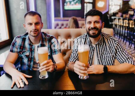 Happy male friends drinking beer and clinking glasses at bar or pub Stock Photo