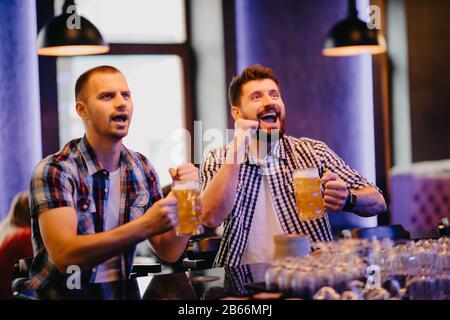 Happy men shouting while watching football match broadcast in pub Stock Photo