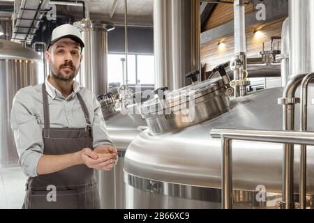 Professional brewer on his own craft alcohol production. Specialist, man wearing in workwear testing raw materials for manufacturing. Concept of open business, eco product, craft brewery, factory. Stock Photo